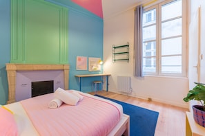 Ein Schlafzimmer mit Bett, Schreibtisch, Heizkörper und einem Fenster mit Vorhängen.