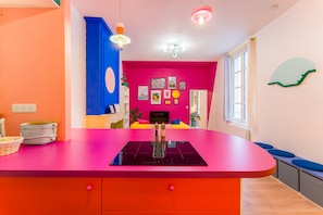 Eine leuchtend farbene Küche mit einer zentralen Kochinsel, einem Essbereich mit einem gelben Sofa und einem Fernseher an der Wand.