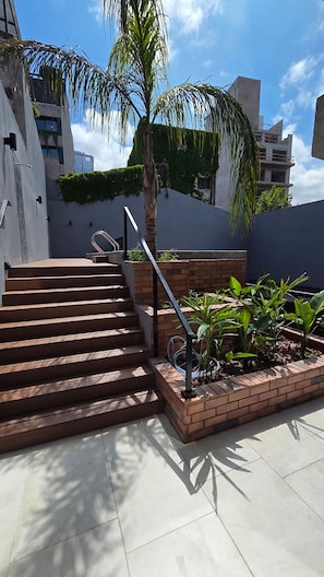 Un escalier extérieur menant à une terrasse sur le toit, agrémentée d’un palmier et d’un parterre de fleurs.