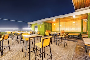 Un espacio al aire libre con mesas y sillas, techo de madera y vista al cielo nocturno.