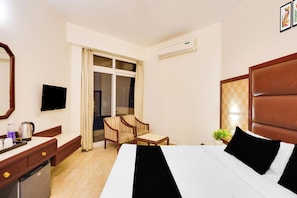 Habitación de hotel con cama, escritorio, silla, televisor y aire acondicionado.