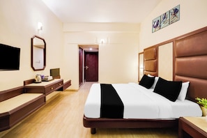 A hotel room with a large bed, a desk, a chair, a flat-screen TV, a mirror, and a door leading to another room.