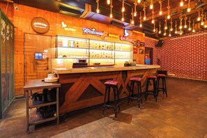 Una zona de bar con mostrador de madera, taburetes y una variedad de botellas de licor.