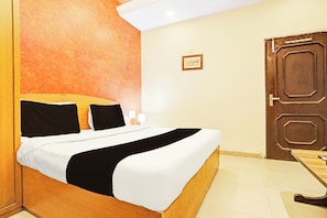 Una habitación de hotel con una cama, una puerta de madera y un cuadro pequeño en la pared.