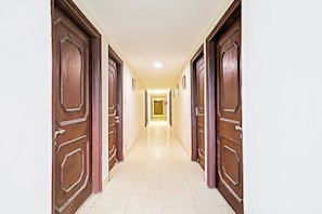 A corridor with wooden doors on both sides, leading to a room with a tiled floor and a ceiling light. - Hotel O Jaistambh Chowk (Raipur)