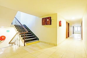 A hotel corridor with a staircase, fire safety equipment, and a fire exit sign. - Hotel O Jaistambh Chowk (Raipur)