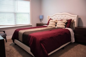 Een slaapkamer met een bed, nachtkastjes, een lamp en een raam met jaloezieën.