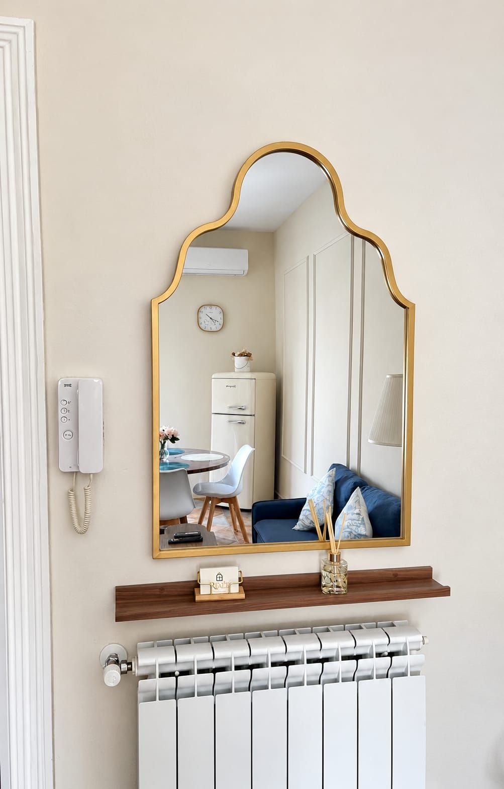 Une salle de bain avec un miroir, un radiateur, un téléphone et une petite table sur laquelle est posé un vase.