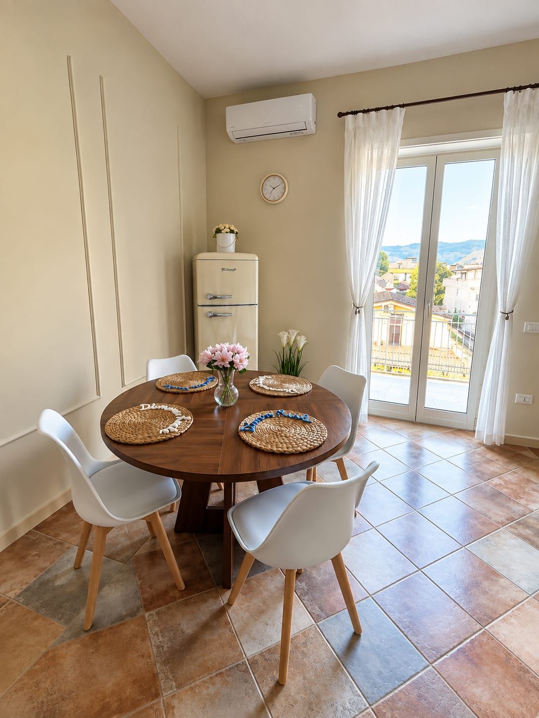 Zona pranzo con tavolo rotondo, sedie bianche e sottopiatti in fibra.
