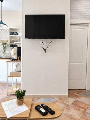 Une cuisine moderne avec un téléviseur à écran plat fixé au mur, une table en bois avec une télécommande, et une plante en pot.