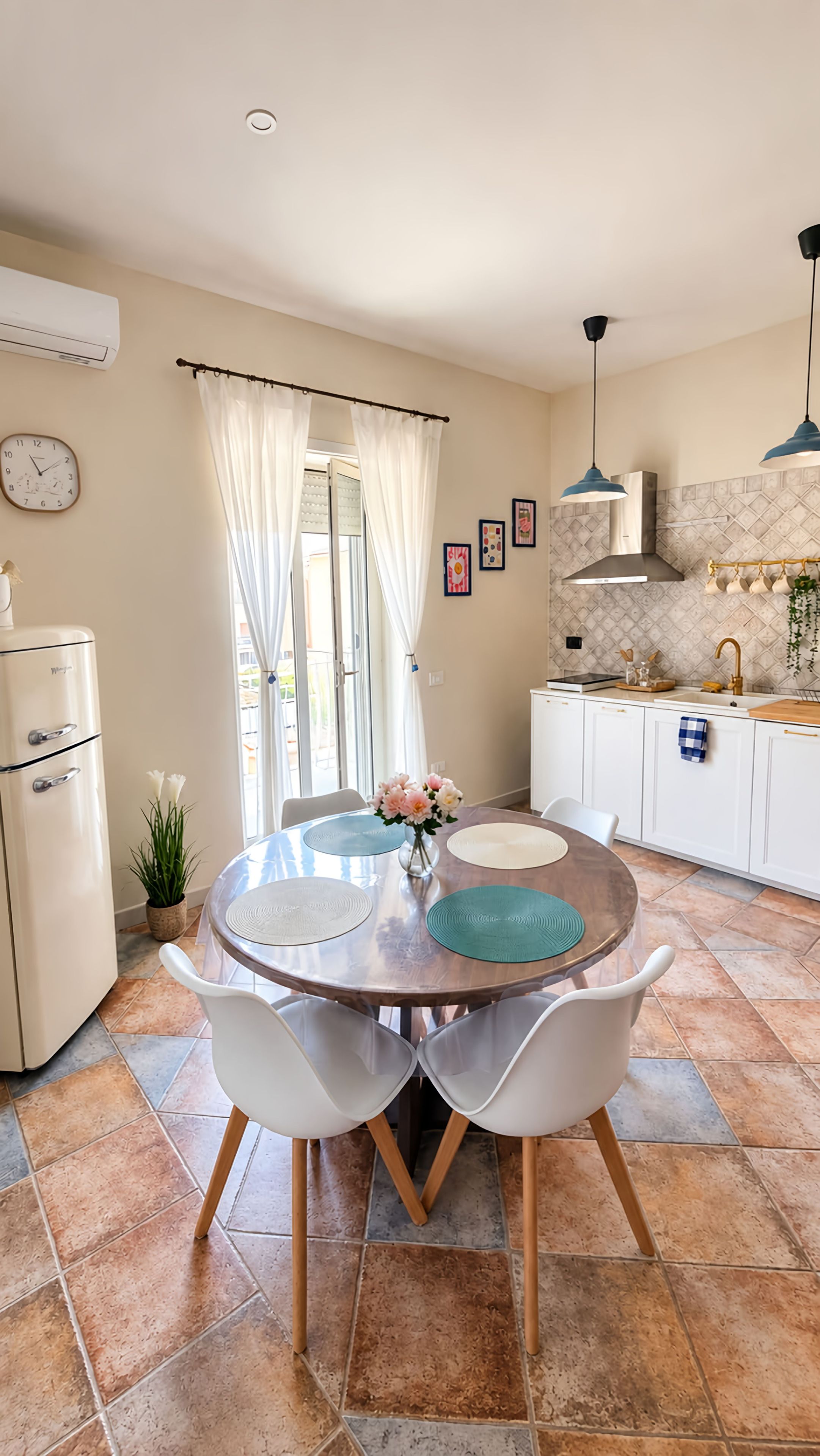 Un coin repas avec une table ronde, des chaises blanches et une cuisine en arrière-plan.