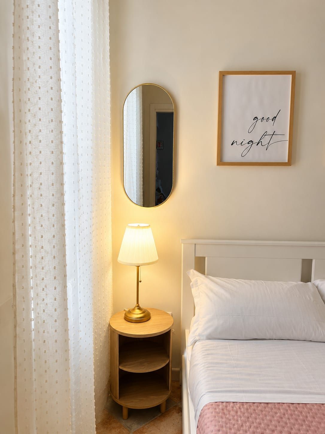 Ein Schlafzimmer mit einem Bett, einer Nachttischlampe, einem Spiegel und einem gerahmten Schild an der Wand.