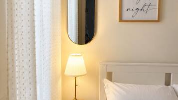 Ein Schlafzimmer mit einem Bett, einer Nachttischlampe, einem Spiegel und einem gerahmten Schild an der Wand.