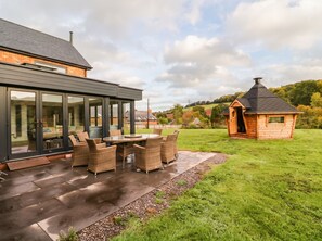 A modern house with a glass-enclosed patio, outdoor furniture, and a small wooden structure. - Hanbury House (Ross-on-Wye)