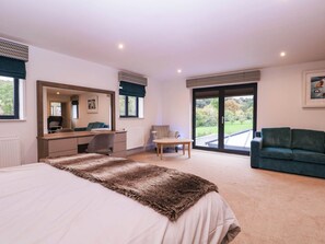 A bedroom with a large bed, a desk, a chair, a sofa, and a view through a glass door. - Hanbury House (Ross-on-Wye)