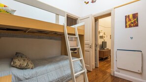 Ein Etagenbett mit einer Leiter, ein kleiner Schreibtisch mit einem Computer und ein Fernseher in einem kompakten Zimmer.