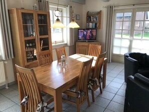 Ein Essbereich mit Holztisch und Stühlen, einem Fernseher und einem Bücherregal.