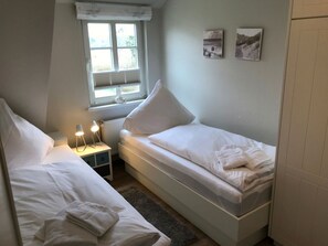 Ein Schlafzimmer mit zwei Einzelbetten, einem Nachttisch mit Lampe, einem Fenster mit Jalousien und zwei an der Wand befestigten Bildern.