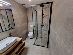 A modern bathroom with a glass-enclosed shower, a white toilet, and a wooden vanity with a sink. - Damian (Pula)