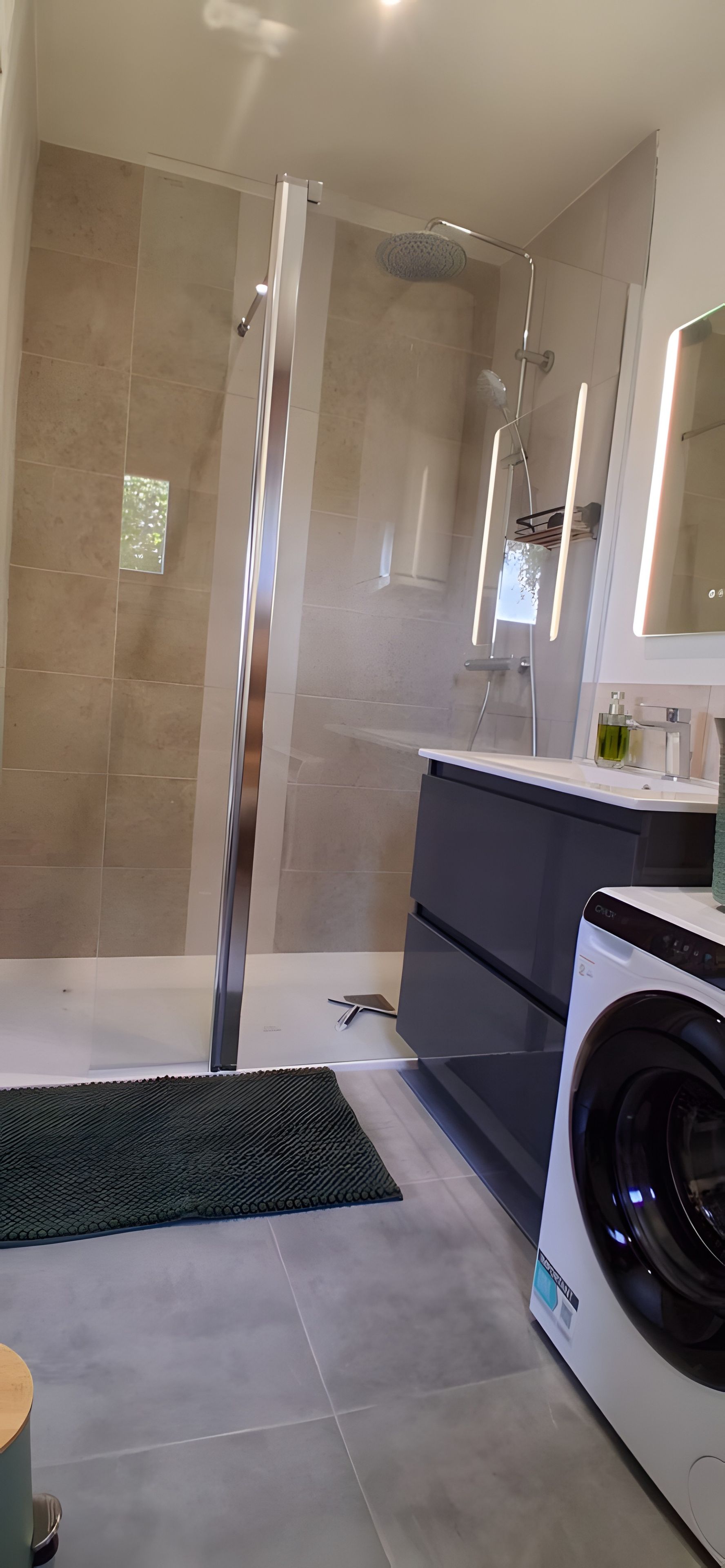 Ein modernes Badezimmer mit Duschkabine aus Glas, einer Waschmaschine und einem großen Spiegel.