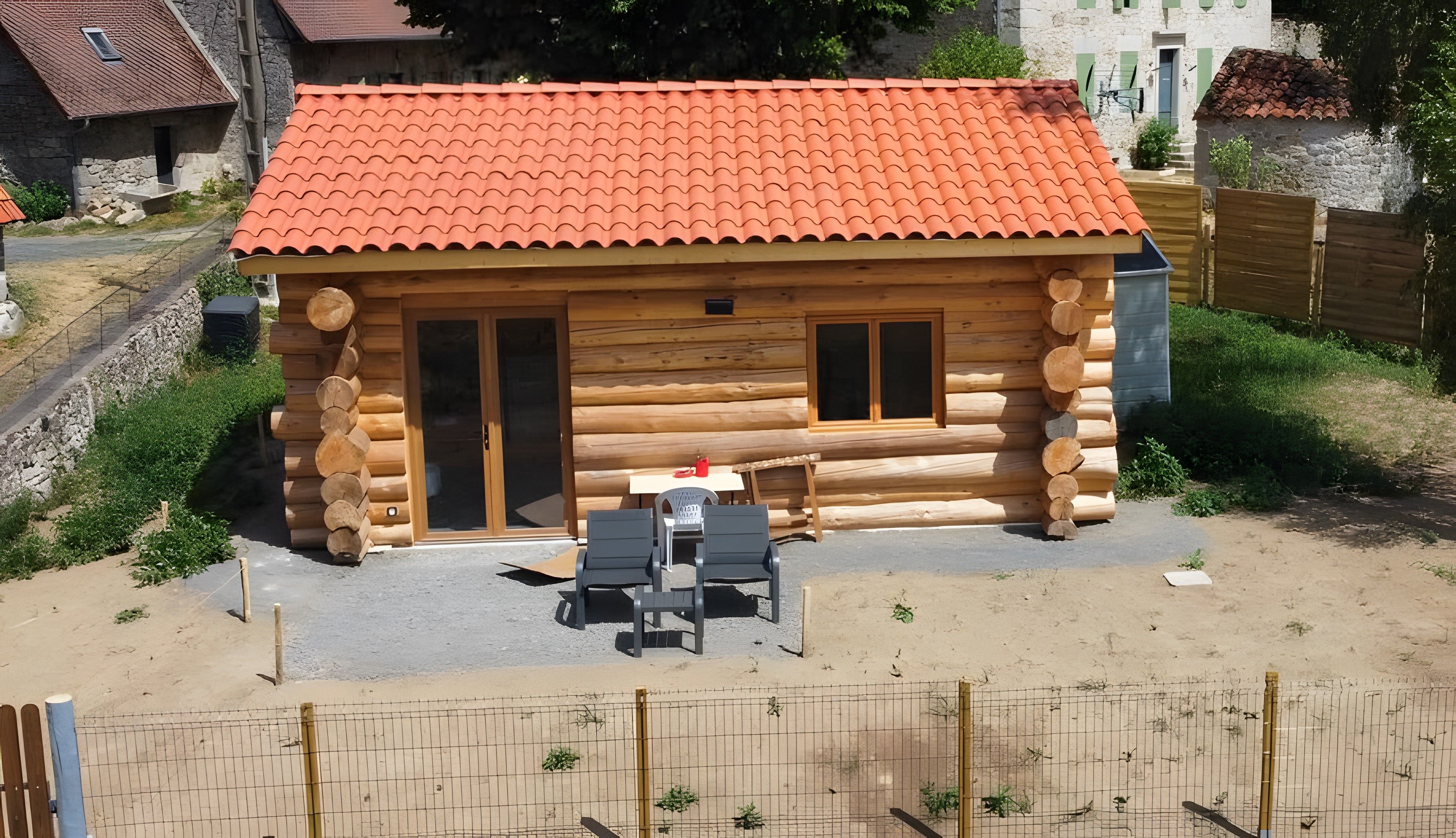 Une cabane en rondins avec un toit en tuiles, une porte en bois et une petite terrasse avec deux chaises et une table.