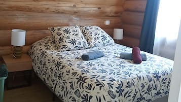 A wooden cabin-style room with a bed, two bedside lamps, and a hanging light fixture.