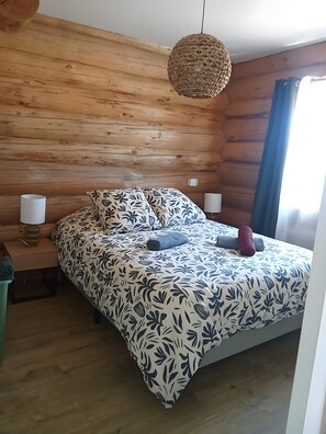 Ein holzgetäfeltes Zimmer im Blockhausstil mit einem Bett, zwei Nachttischlampen und einer Hängeleuchte.