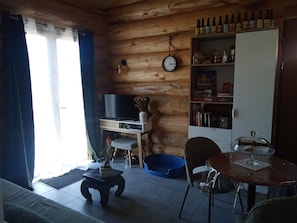 Un salon chaleureux avec un décor intérieur en bois, un téléviseur à écran plat, une petite table ornée d’un vase et une bibliothèque contenant divers objets.