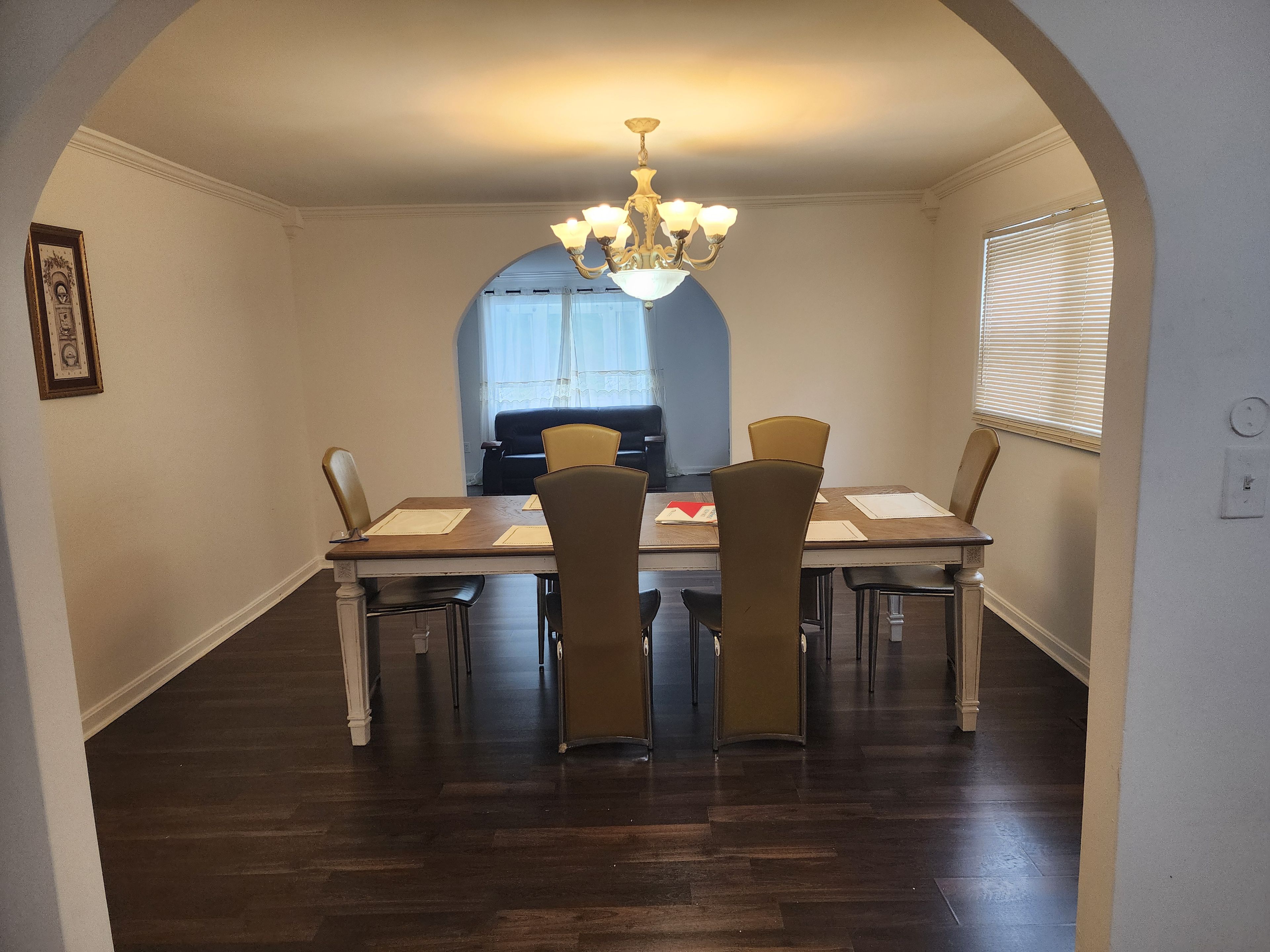 A dining area with a chandelier, a table with chairs, and a window with blinds.