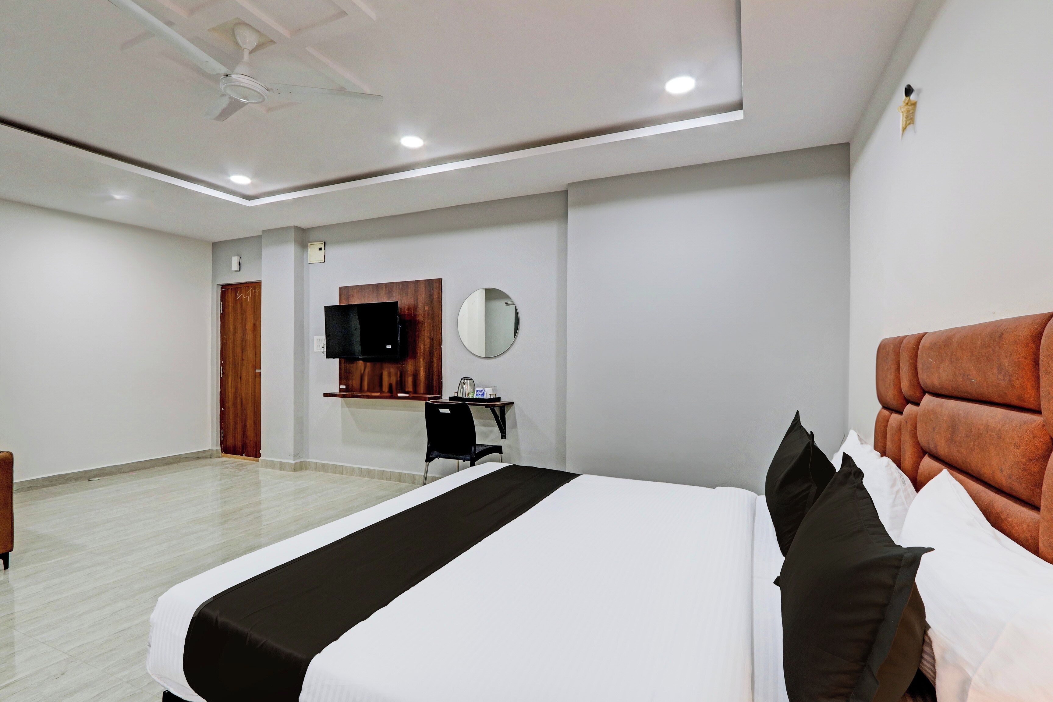 A hotel room with a bed, a desk, a chair, a television, and a ceiling fan.