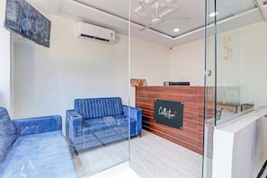 A reception area with a glass partition, a reception desk, a blue sofa, and an air conditioning unit. - Hotel O Lavish Tranquil (Hyderabad)