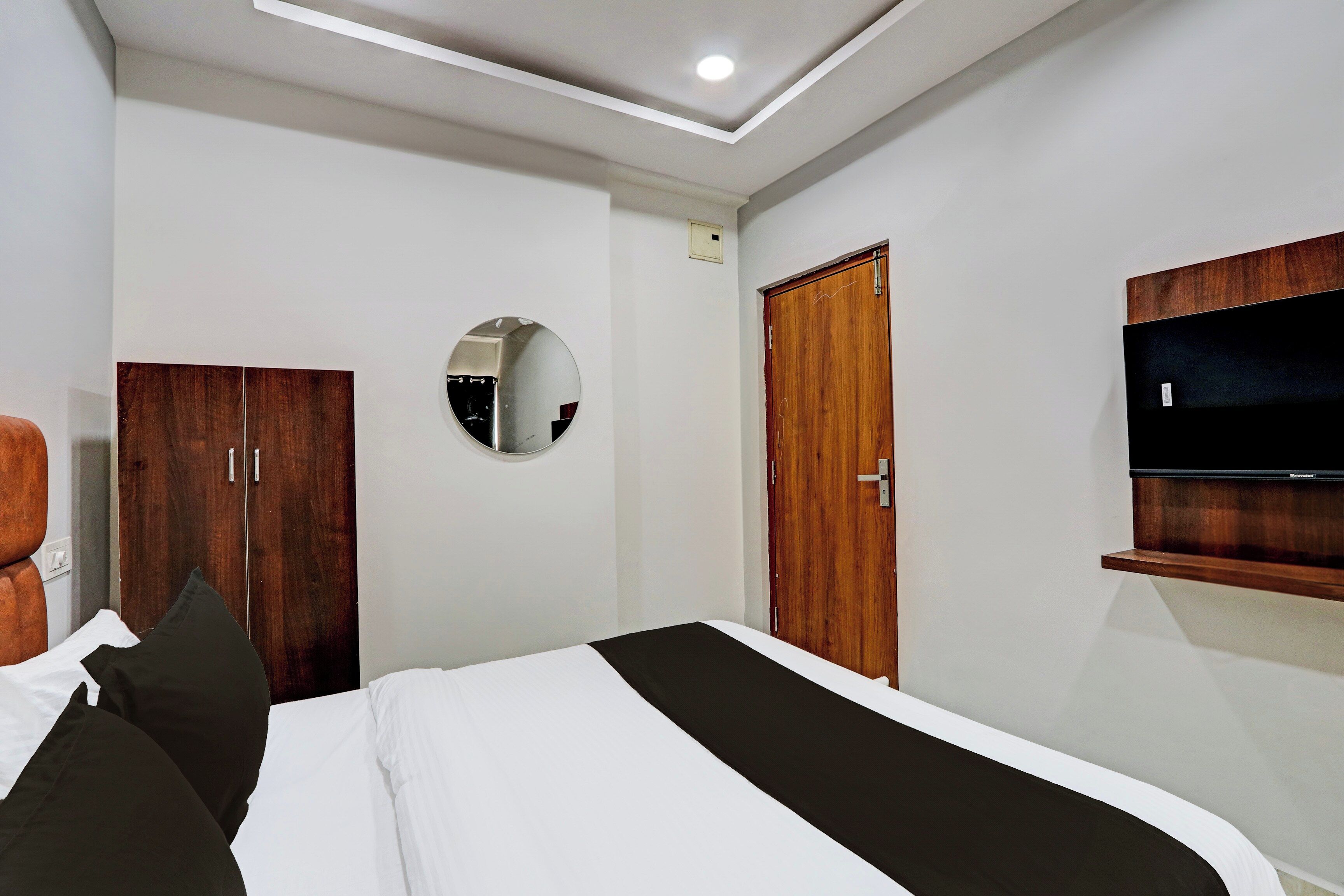 Ein Hotelzimmer mit einem Bett, einem Kleiderschrank, einem Spiegel und einem an der Wand befestigten Fernseher.