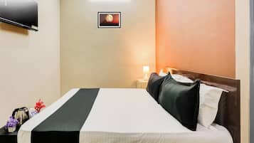 Quarto de hotel com cama, mesa de cabeceira, luminária, televisão e quadro na parede.