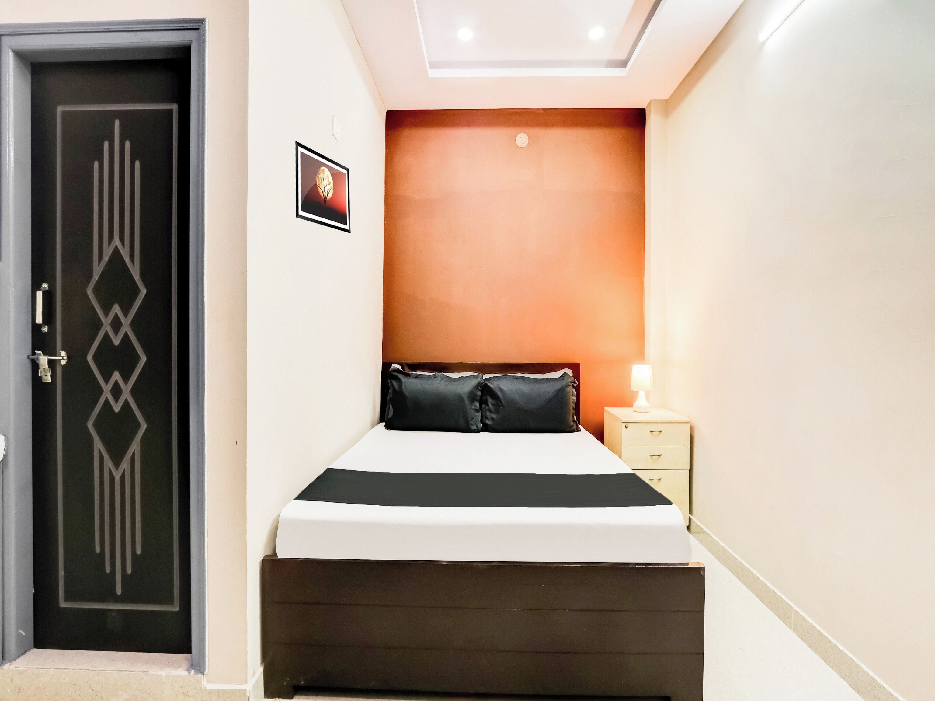 A bedroom with a bed, a nightstand, a wall-mounted light, and a door with a geometric design.