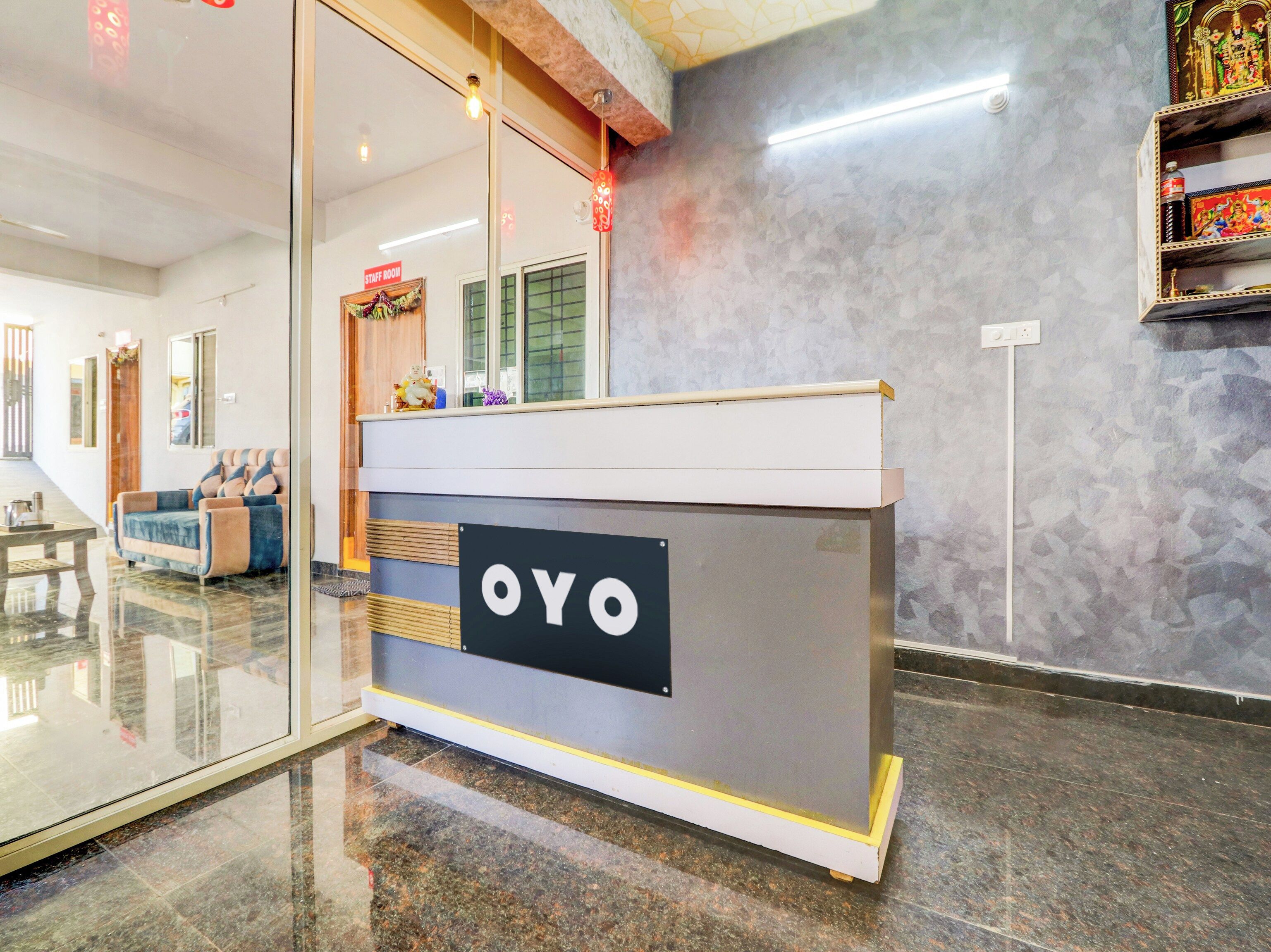 A reception desk with a sign that reads 'OYO' in a hotel lobby with a marble floor, a sofa, and a decorative wall.
