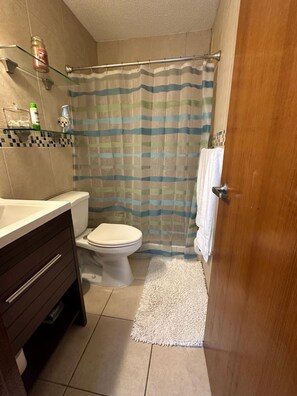 A bathroom with a toilet, shower curtain, and a wooden door. - Beachfront apartment in Luquillo, Puerto Rico!! (Luquillo)
