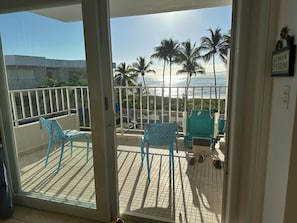 A balcony with chairs and a table, a view of the ocean, and palm trees. - Beachfront apartment in Luquillo, Puerto Rico!! (Luquillo)