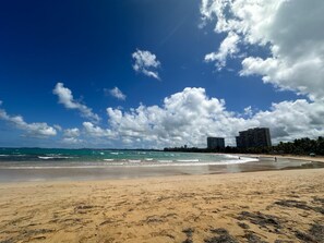 A beach with clear skies, ocean waves, and buildings in the background. - Beachfront apartment in Luquillo, Puerto Rico!! (Luquillo)