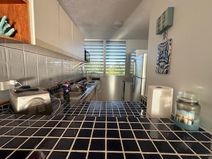 A kitchen with a black and white tiled floor, a toaster, a refrigerator, and a window with blinds. - Beachfront apartment in Luquillo, Puerto Rico!! (Luquillo)