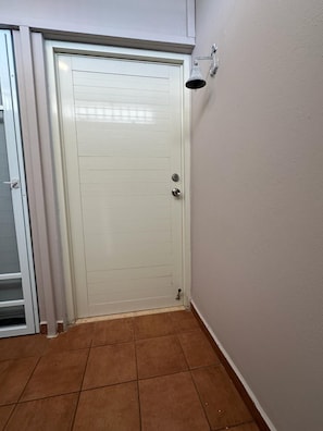 A closed white door with a metal handle and a keyhole, a metal bell on the wall, and a tiled floor. - Beachfront apartment in Luquillo, Puerto Rico!! (Luquillo)