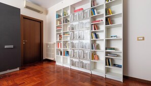 A room with a wooden floor, a white bookshelf filled with books, a radiator, and a closed door. - Italianway Easy - Sismondi 74 (Milan)