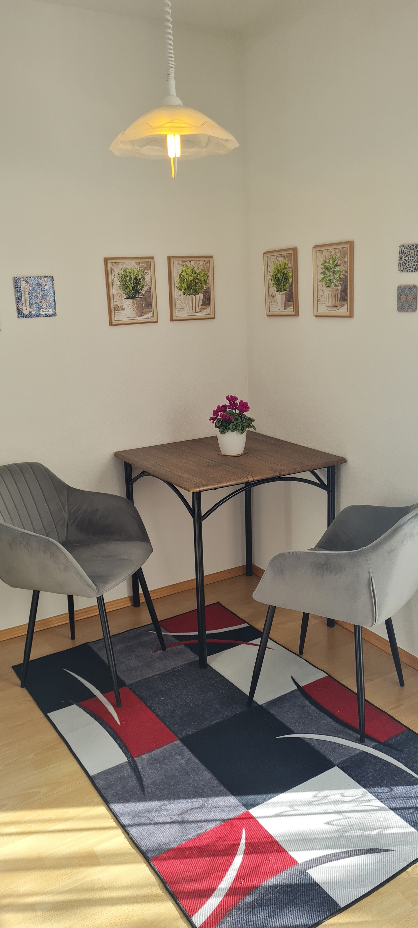 Ein Essbereich mit Tisch, vier Stühlen, einer Hängeleuchte und Wandbildern von Pflanzen.