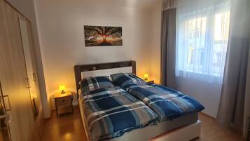Ein Schlafzimmer mit einem Bett, zwei Nachttischlampen, einem Wandbild und einem Fenster mit Vorhängen.