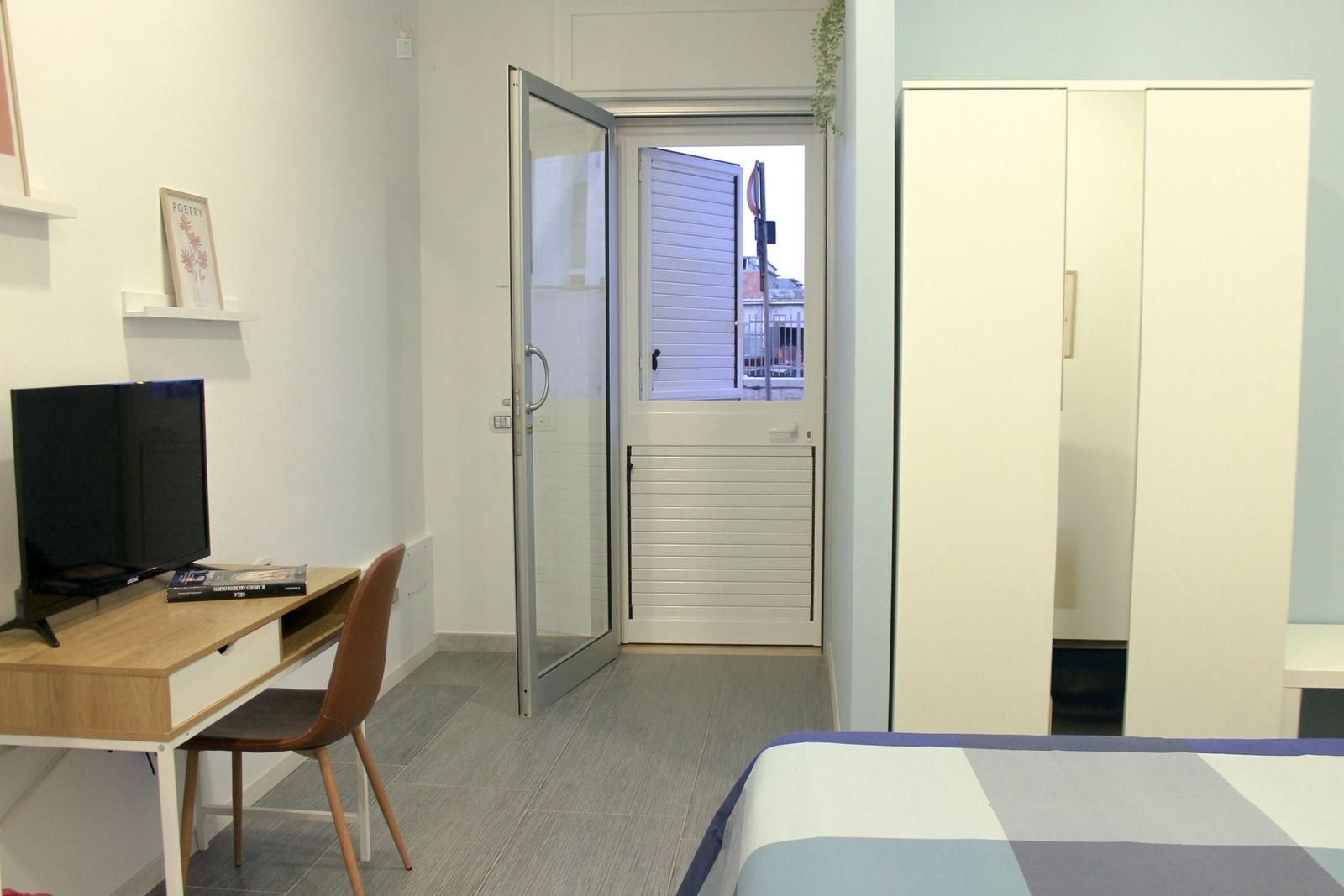 Une chambre d’hôtel comprenant un lit, un bureau avec une chaise, une télévision et une porte coulissante donnant sur un espace extérieur.