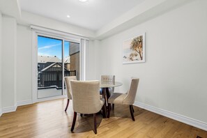A dining area with a round table and four chairs, a large window with a view of buildings, and a framed picture on the wall. - Bright Oakville 3BR Home, Family + Patio & Parking (Oakville)