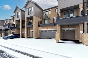 A multi-story residential building with a garage on the ground floor, a car parked in the driveway, and snow on the ground. - Bright Oakville 3BR Home, Family + Patio & Parking (Oakville)