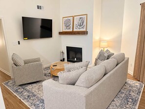 A living room with a sofa, a television, a fireplace, and framed artwork on the wall. - Golf Club Hideaway (Oxford)