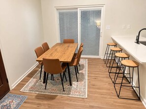 A dining area with a wooden table and chairs, a patterned rug, a kitchen counter with stools, and a sliding glass door. - Golf Club Hideaway (Oxford)