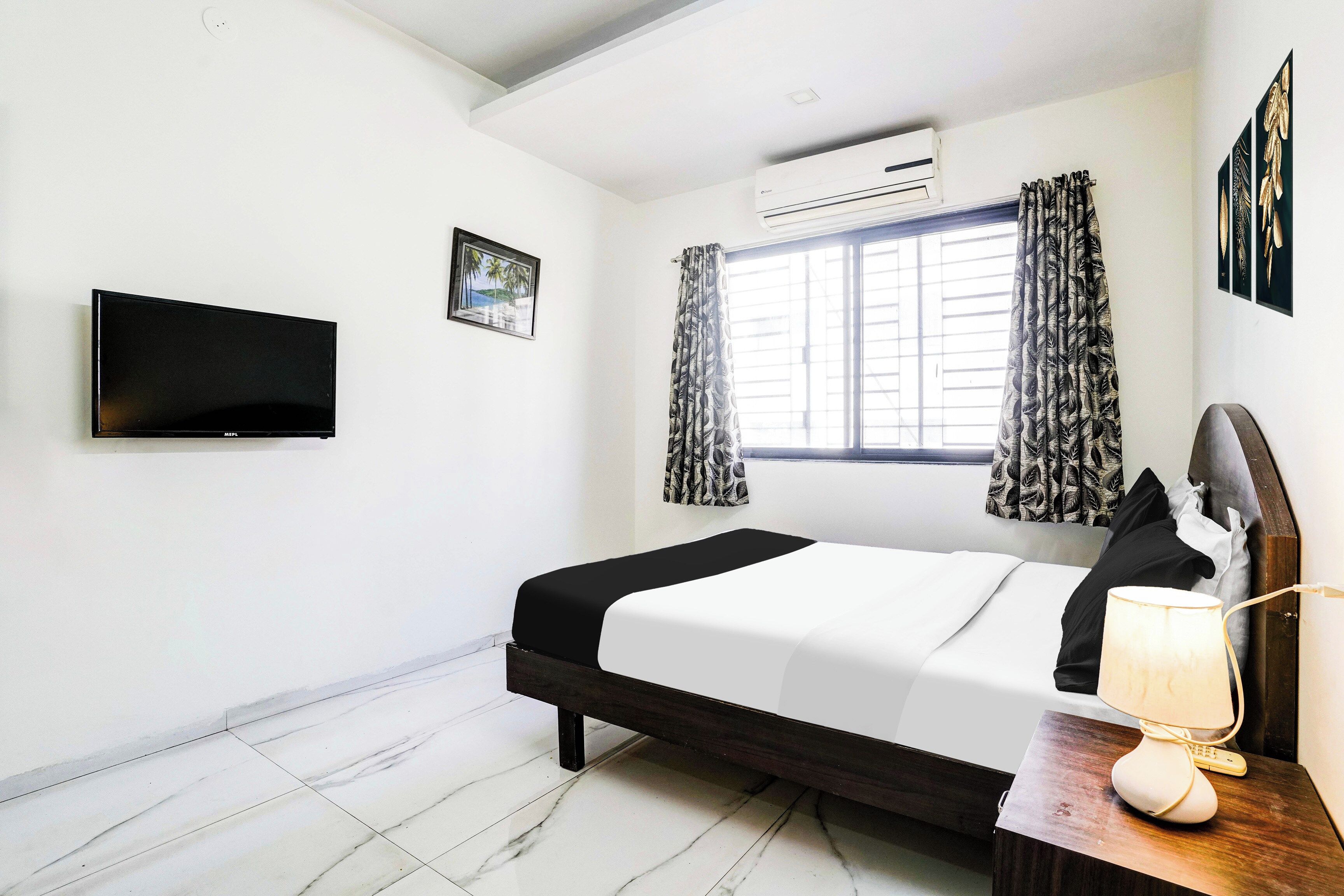 Quarto de hotel com cama, televisão de tela plana, ar-condicionado, janela com cortinas e um quadro na parede.