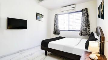 Quarto de hotel com cama, televisão de tela plana, ar-condicionado, janela com cortinas e um quadro na parede.
